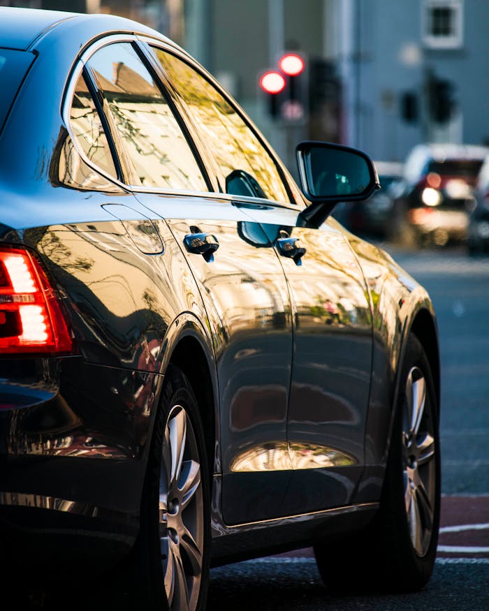 our-experience A shiny black car parked on a city street, reflecting urban surroundings.