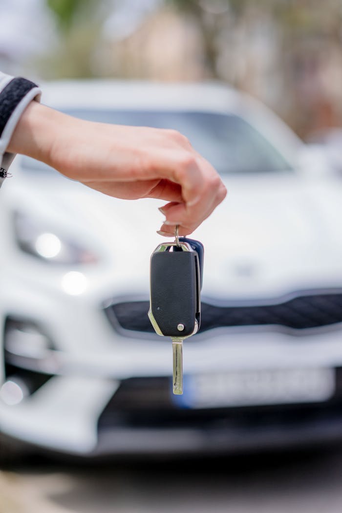 ours-journey Close-up of a hand holding a car key, with a white car in the background outdoors.