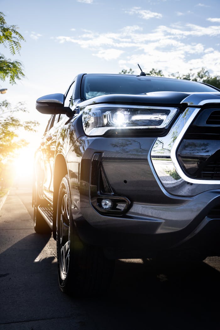 services-03 A sleek Toyota Hilux pickup truck with headlights on, captured at sunset showcasing a modern design.