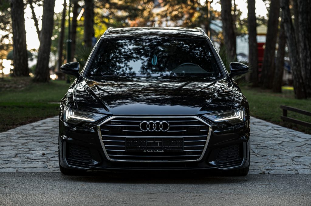 Export Luxury black car parked on a path in a tranquil forest setting, showcasing modern elegance.